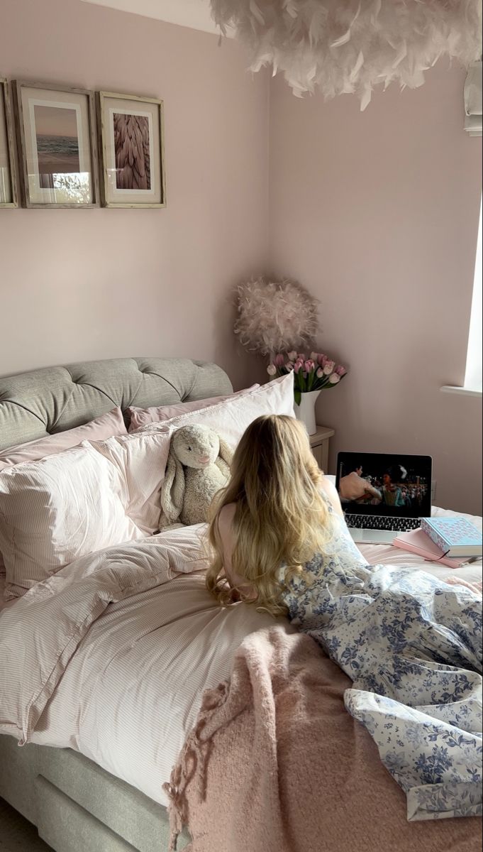 a woman sitting on top of a bed next to a teddy bear in a pink room