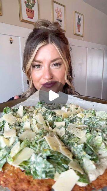 a woman holding up a pizza with cheese and spinach toppings on it in front of her face