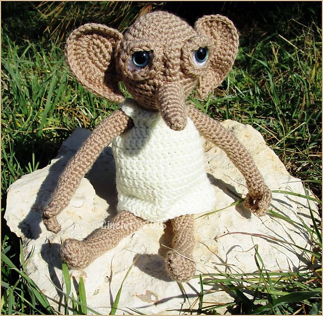 a crocheted stuffed animal sitting on top of a rock in the grass with eyes wide open