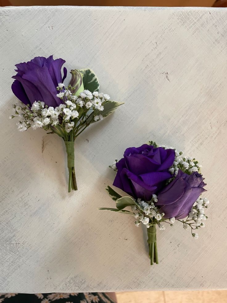 two purple flowers sitting on top of a white table next to each other and baby's breath