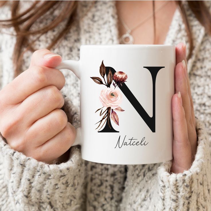 a woman holding a white coffee mug with the letter n on it and pink flowers