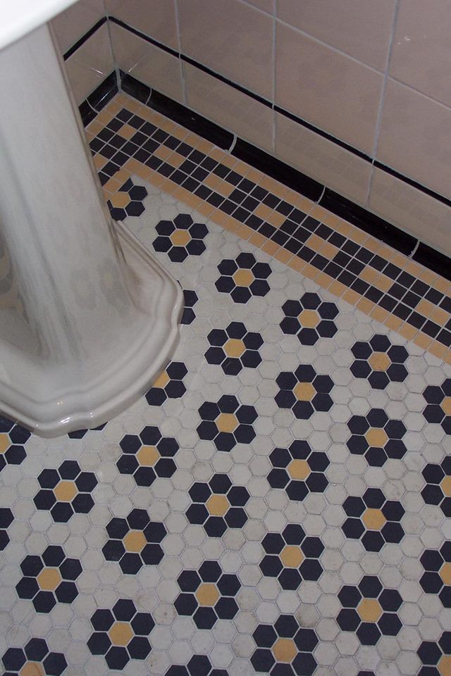 a bathroom with black and yellow tiles on the floor, toilet seat cover and pedestal