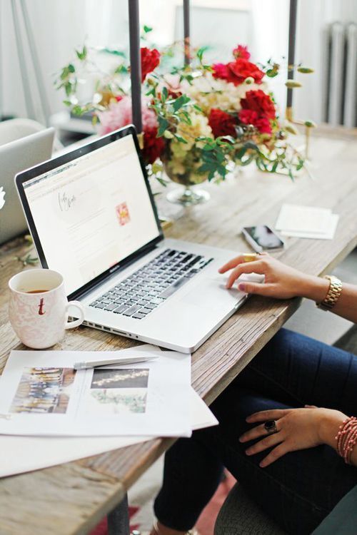 a woman sitting in front of a laptop computer on top of a wooden table with flowers