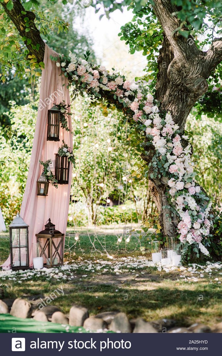 an outdoor ceremony setup with pink and white flowers on the arbor, hanging from a tree