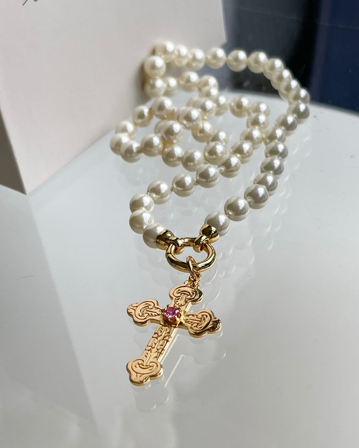 Bernadette Necklace, from our French Rivera Collection. Adorned with a cross pendant, hand-knotted pearls add a touch of elegance to any outfit. 18k Gold plated silver cross 22x31mm with pink cubic zirconia stone 3mm Pearl Shell hand knotted pearls 17 inches long. Hand Knotted Pearls, Pearl Shell, Silver Cross, Gold Plated Silver, Cross Pendant, Silver Plate, Hand Knotted, Cubic Zirconia, 18k Gold