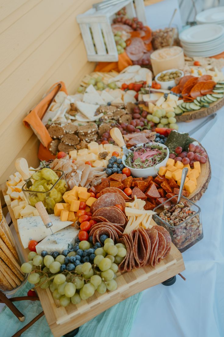 an assortment of cheeses, meats and vegetables on a wooden platter at a buffet table