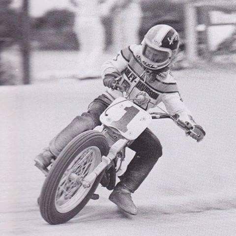 a man riding on the back of a motorcycle down a race track in black and white