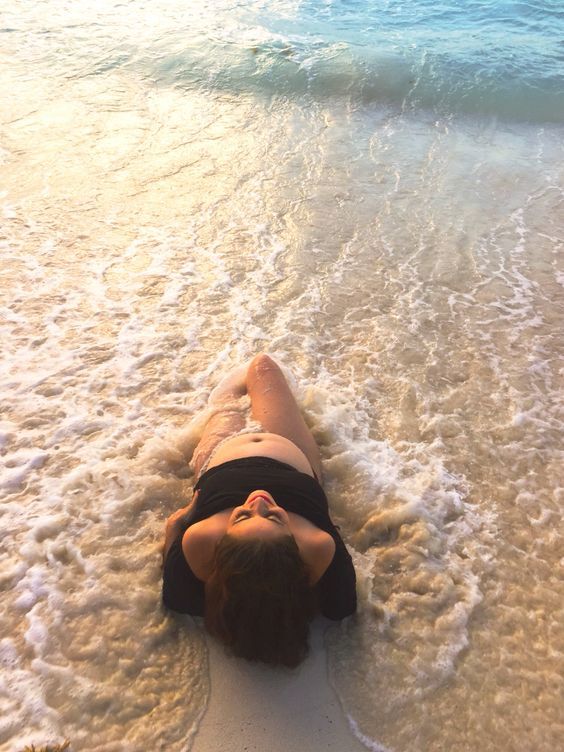 a woman laying on top of a sandy beach next to the ocean with her eyes closed