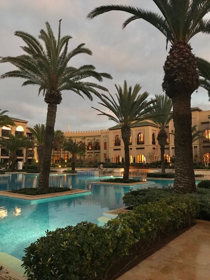 palm trees are in front of a large swimming pool at the resort's entrance