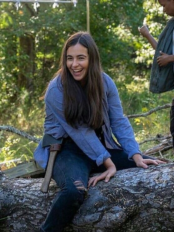 a woman sitting on top of a tree branch in the woods smiling at the camera