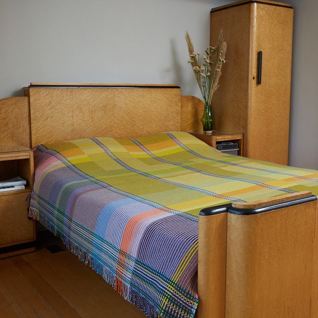 a bed with a plaid blanket on top of it next to a wooden dresser and cabinet