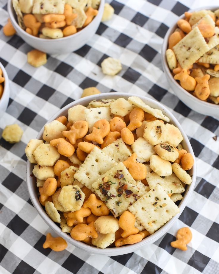 two bowls filled with crackers and nuts on a checkered table cloth next to other snacks