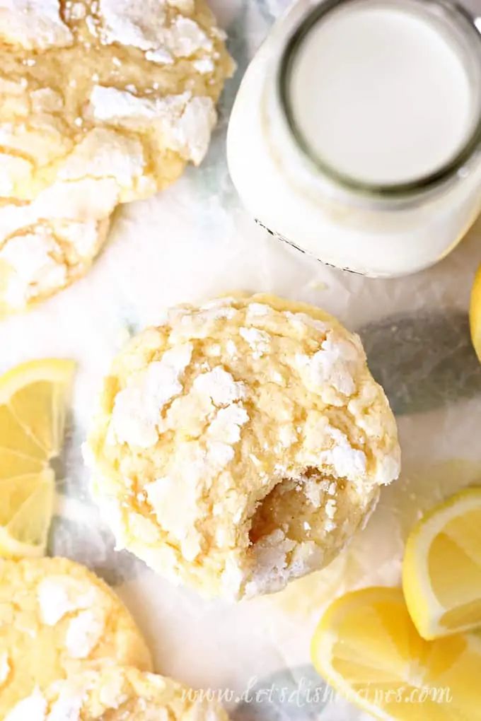 lemon cookies with powdered sugar on top next to sliced lemons and a glass of milk