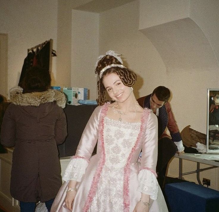 a woman in a pink and white dress standing next to a man wearing a brown coat