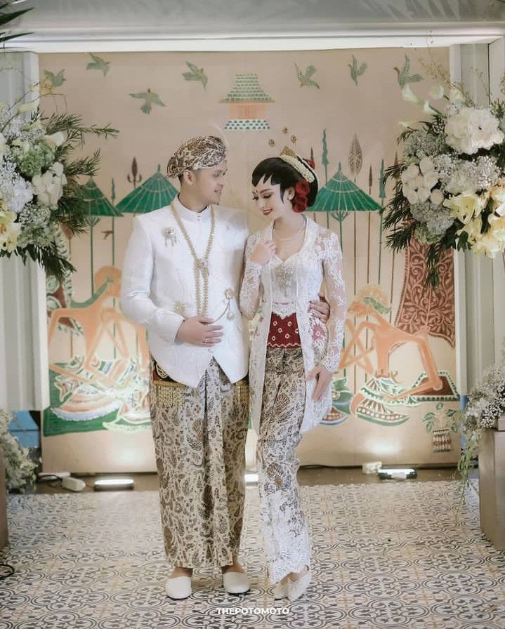 a man and woman standing next to each other in front of a wall with flowers