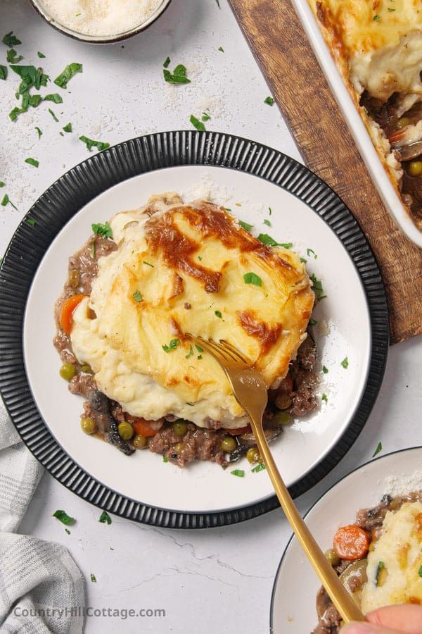 a person is holding a fork over a plate of shepherd's pie