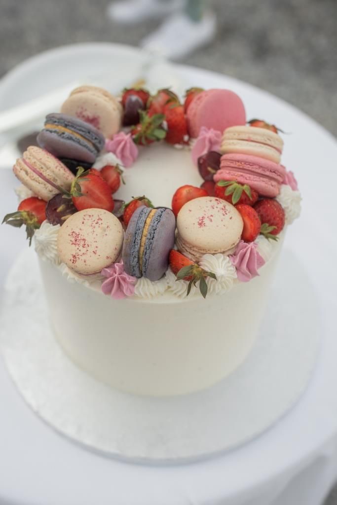 a white cake topped with lots of different types of macaroons and strawberries