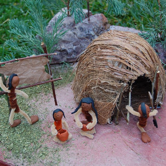 some figurines are standing in front of a small hut with grass and trees