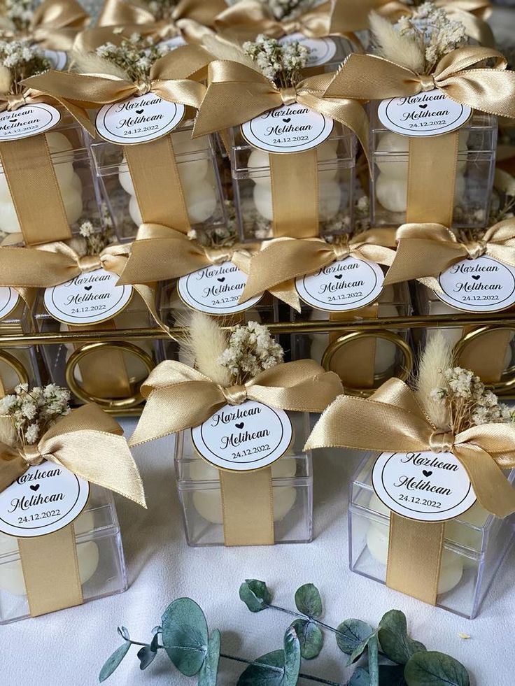 wedding favors in clear boxes with gold ribbons and tags on them are sitting next to each other