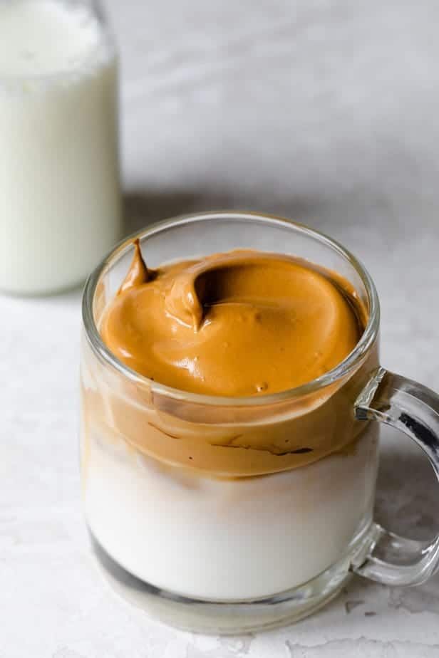 a glass mug filled with pudding next to a bottle of milk on a white surface