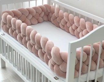 a white crib with pink pillows in the shape of circles on it's sides