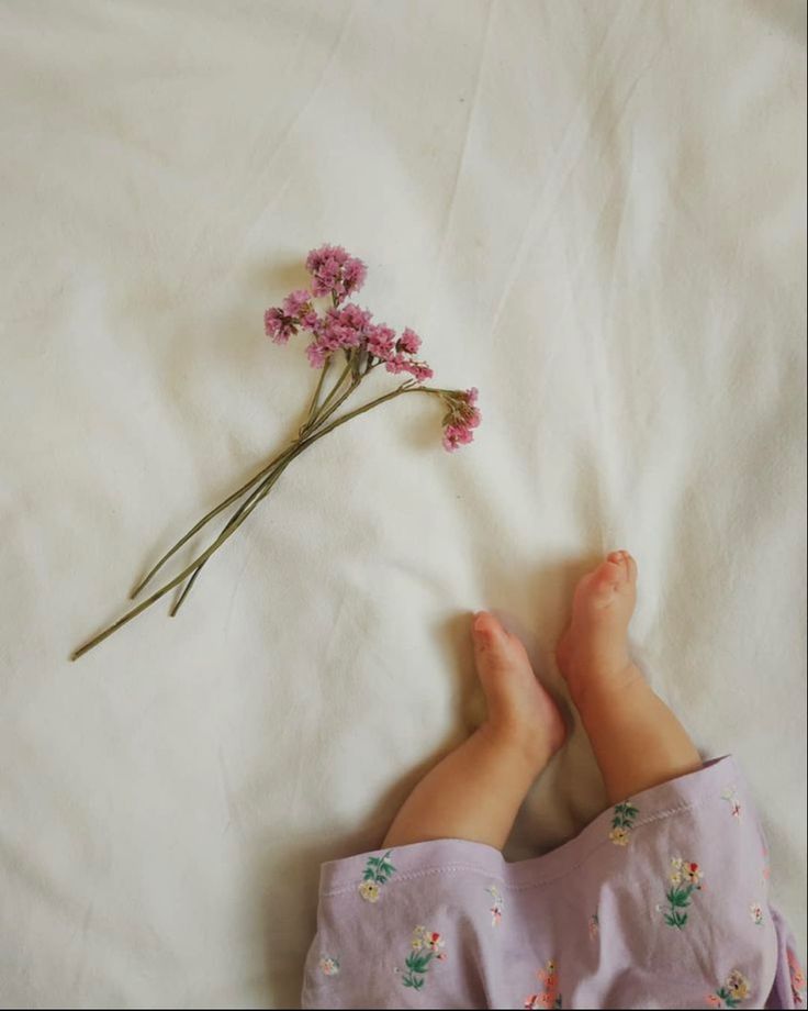 the baby is laying down with her feet on the bed next to some pink flowers