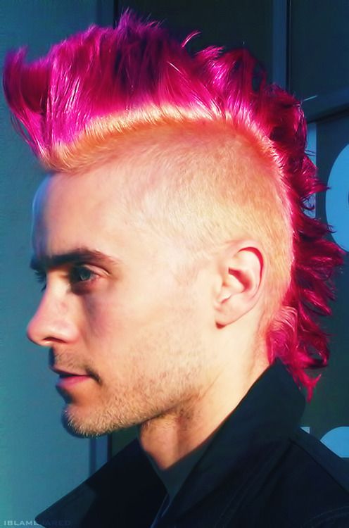 a young man with pink hair and spiked mohawk looks off to the side while wearing a black shirt