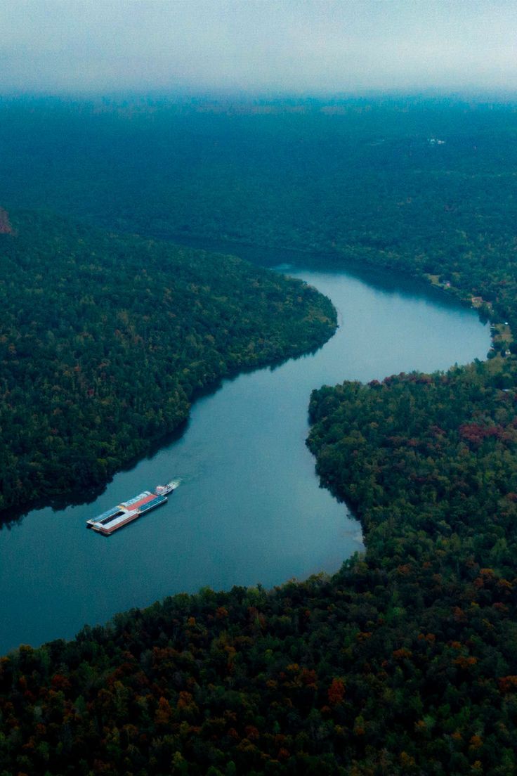 a large boat floating on top of a river surrounded by forest