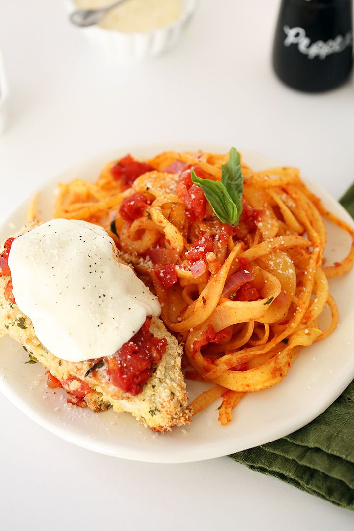 a white plate topped with spaghetti and meat covered in tomato sauce next to a bottle of wine