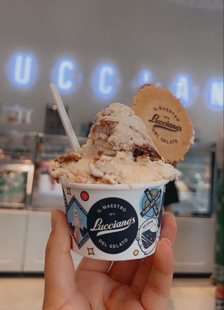 a hand holding an ice cream sundae in front of a sign that reads ucccia