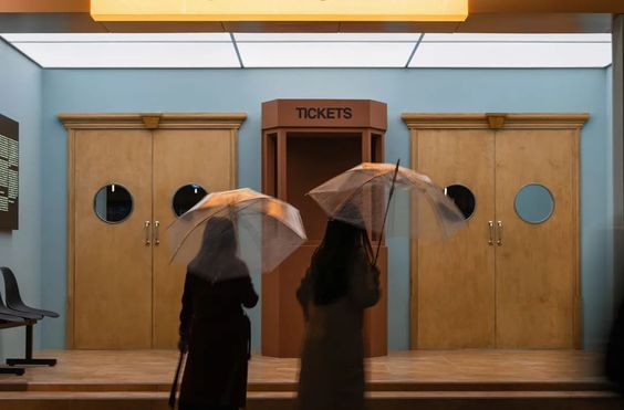 two women with umbrellas are standing in front of lockers at the ticket booth