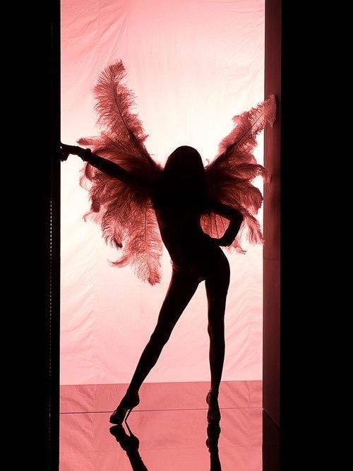 a woman is standing in front of a pink background with wings on her body and arms outstretched