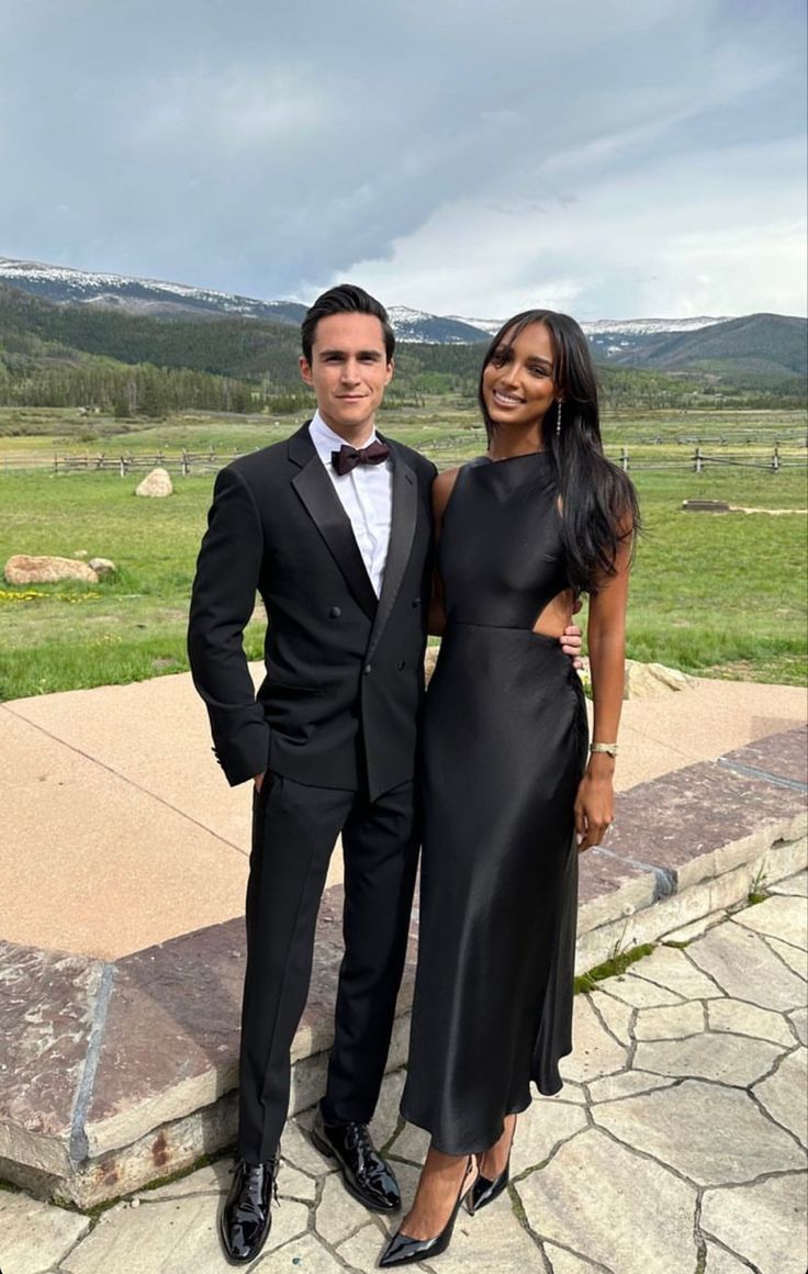 a man and woman in formal wear posing for a photo on the side of a stone wall