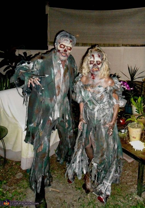 two people dressed as zombies walking in the yard at night time with decorations on them