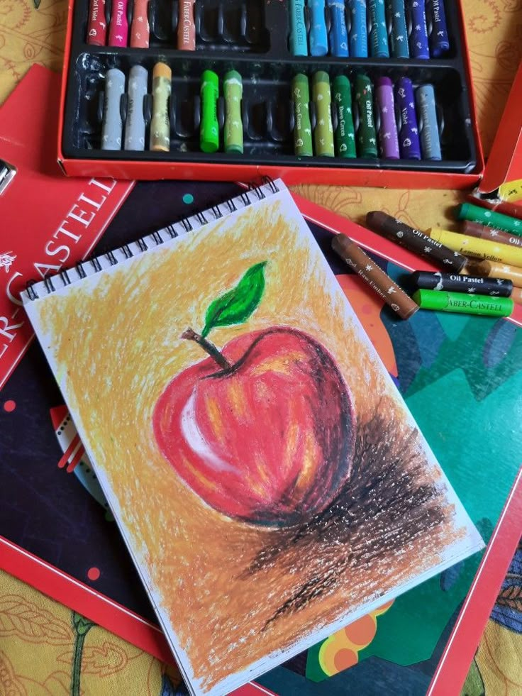 an apple drawn on paper next to some crayons and colored pencils in a box