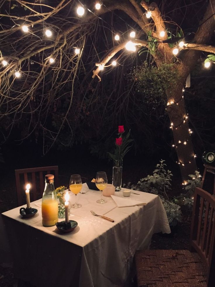 an outdoor dining area with lights strung from the tree and candles lit on the table