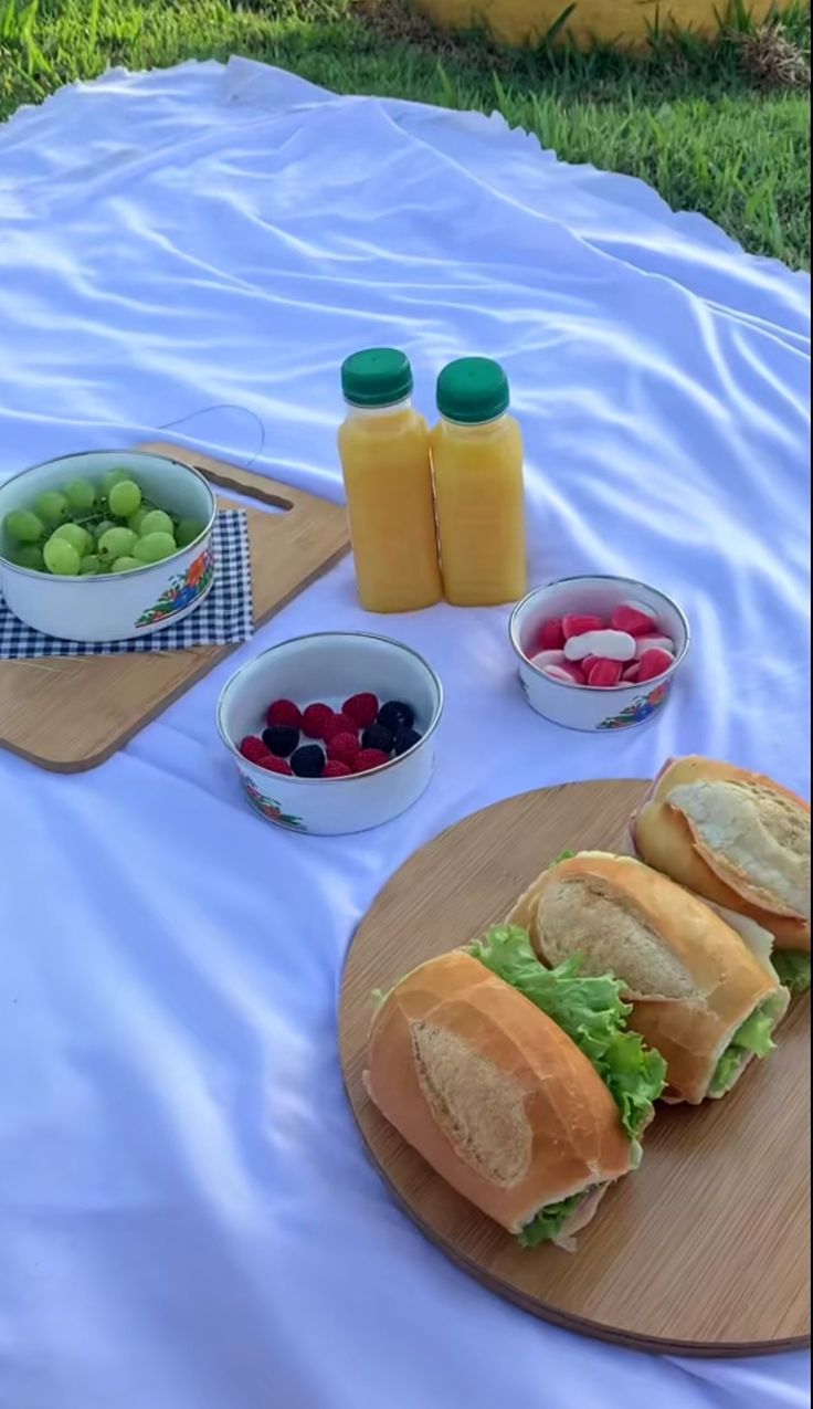 two sandwiches are on a cutting board with fruit and juices in the bowl next to them