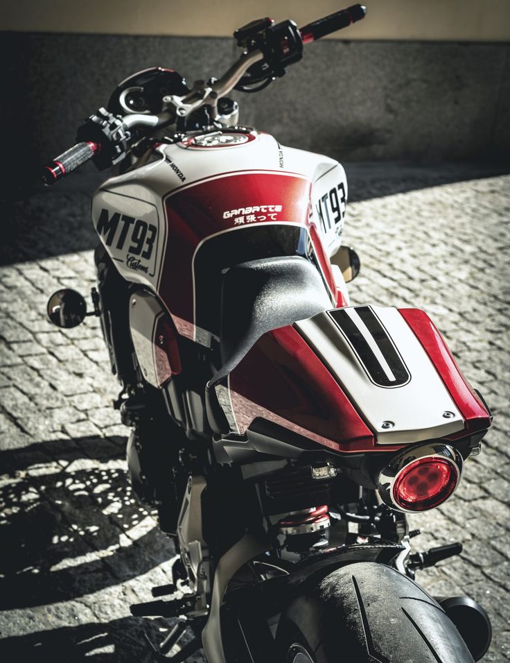 a red and white motorcycle parked on top of a brick road