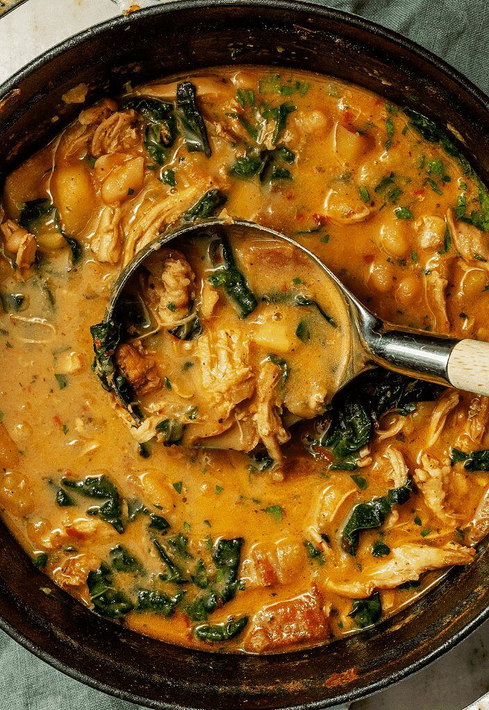 a large pot filled with chicken and spinach in gravy, topped with a wooden spoon