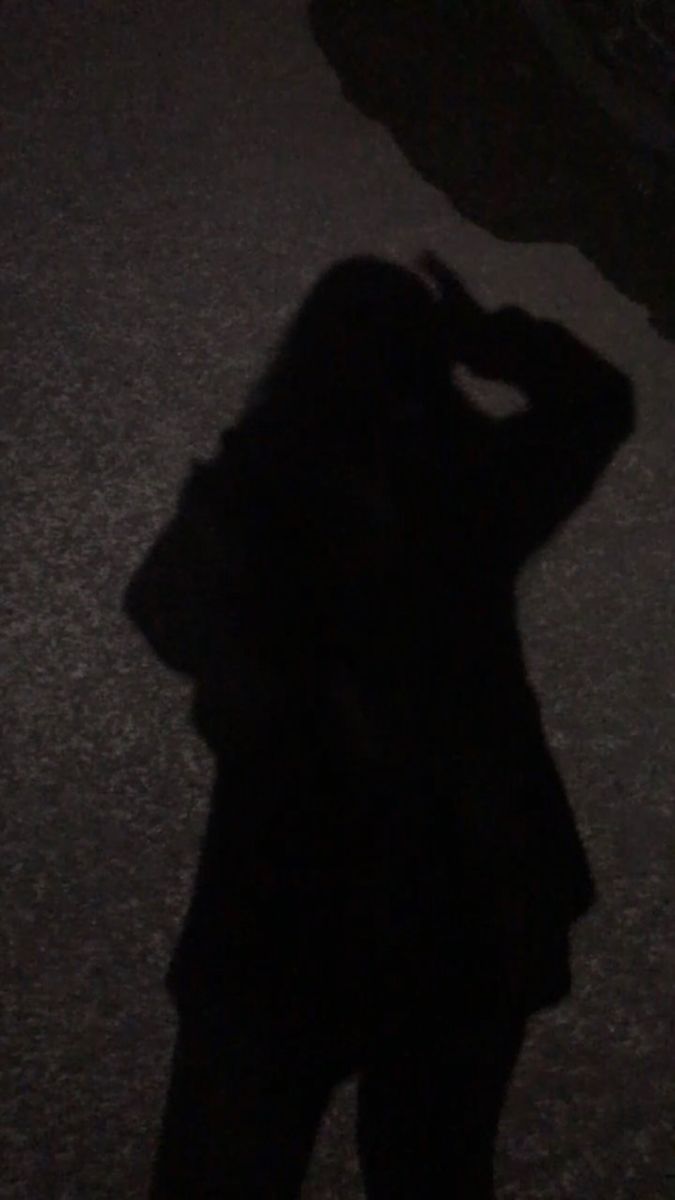 a person standing in the dark with their shadow on the ground and holding an umbrella