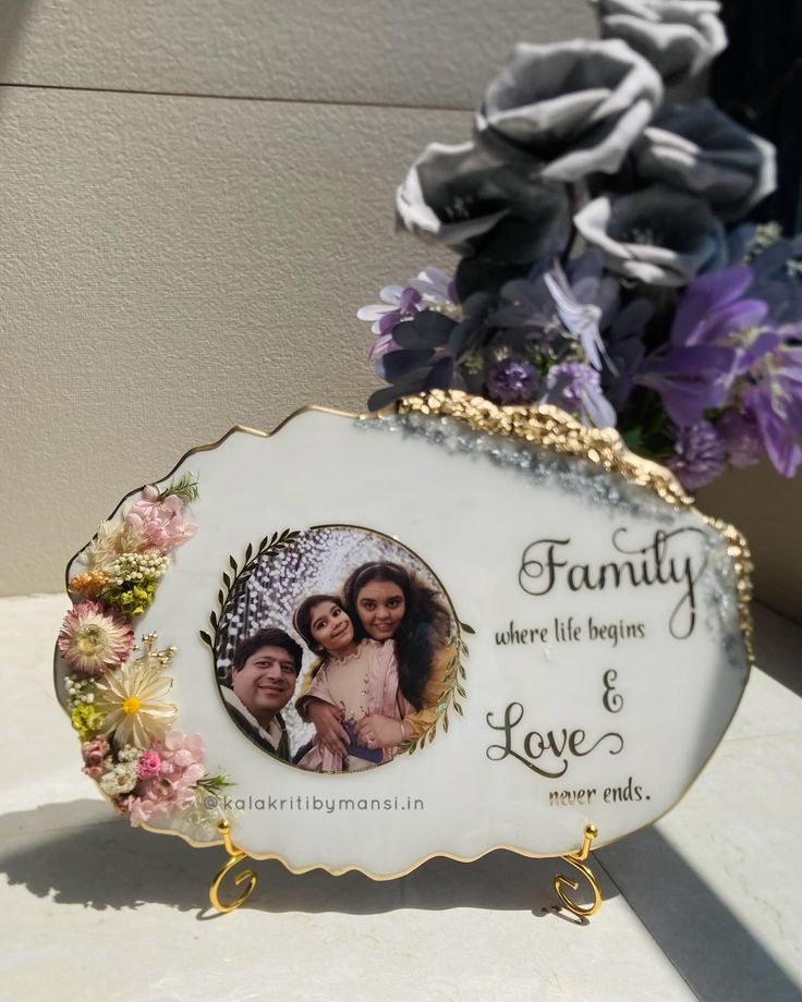 a white and gold frame sitting on top of a table next to purple flowers in a vase