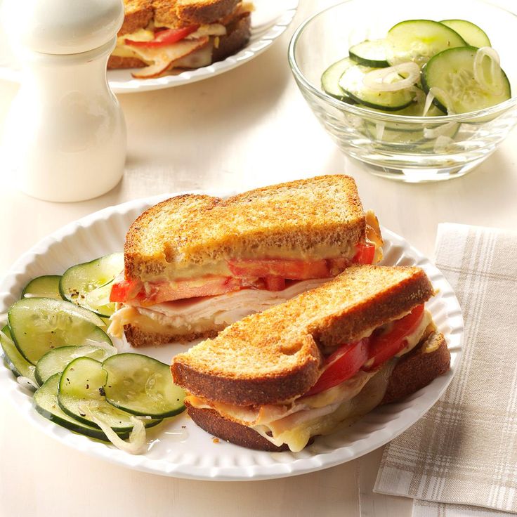 two plates with sandwiches and cucumbers sitting on a table next to each other