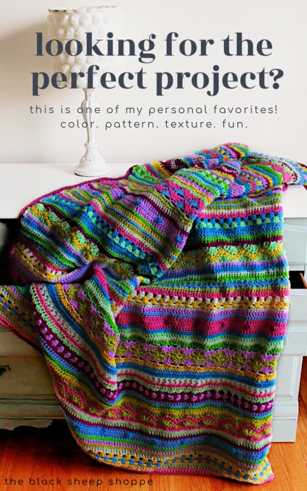 a colorful crocheted blanket sitting on top of a white dresser next to a lamp