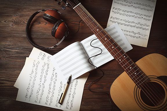 an acoustic guitar, headphones and music sheets on a wooden table with sheet music