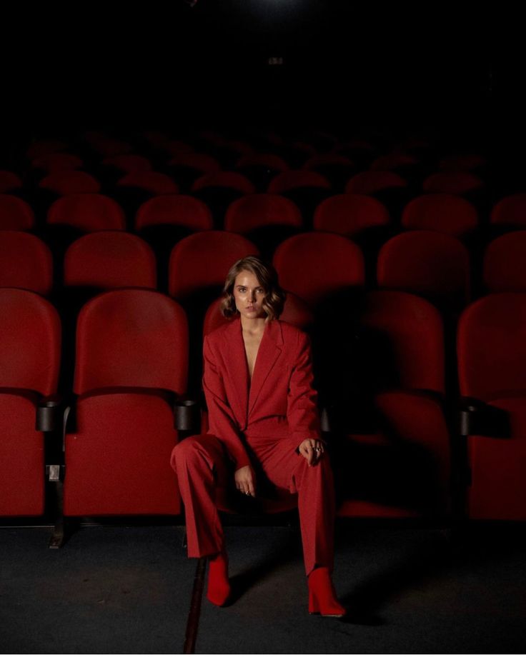 a woman in a red suit sitting on a chair next to an empty theater seat