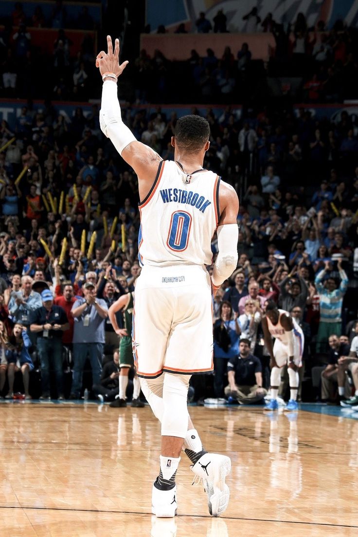 a basketball player walking on the court with his hand in the air and people watching