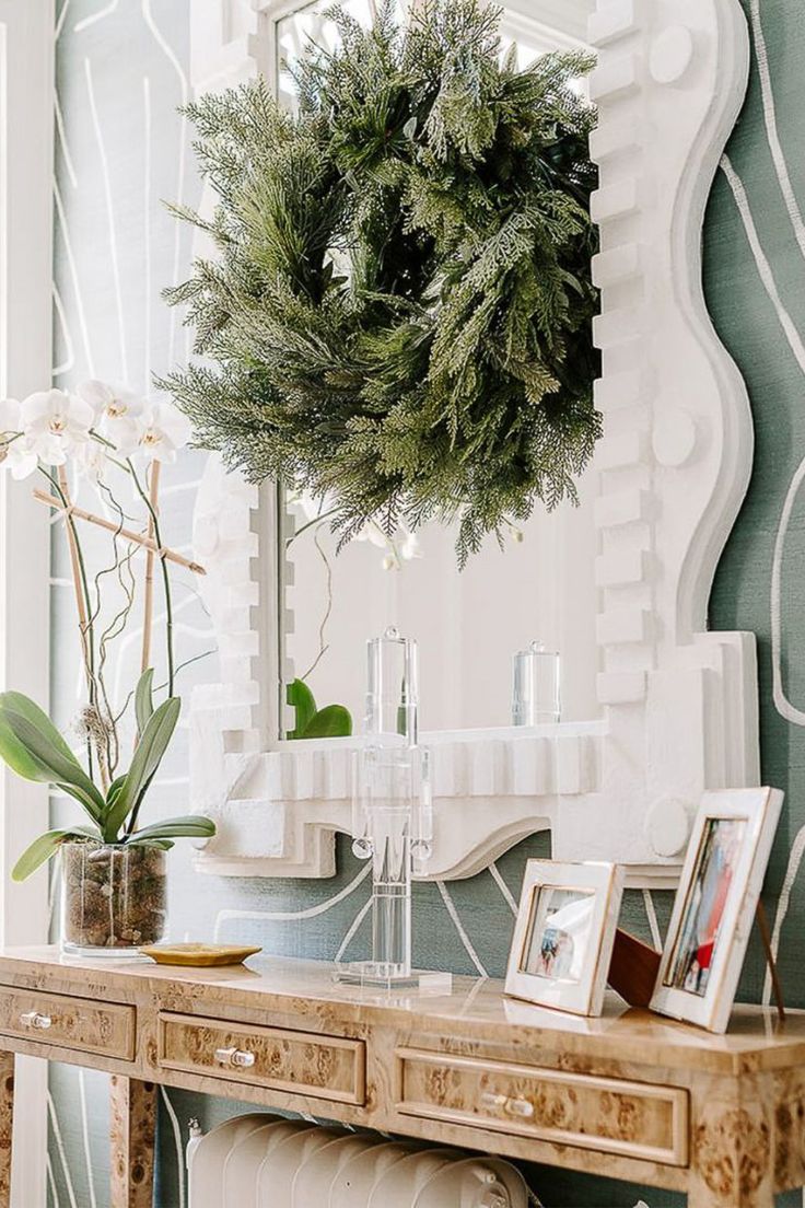 a table with pictures and plants on it in front of a wallpapered mirror