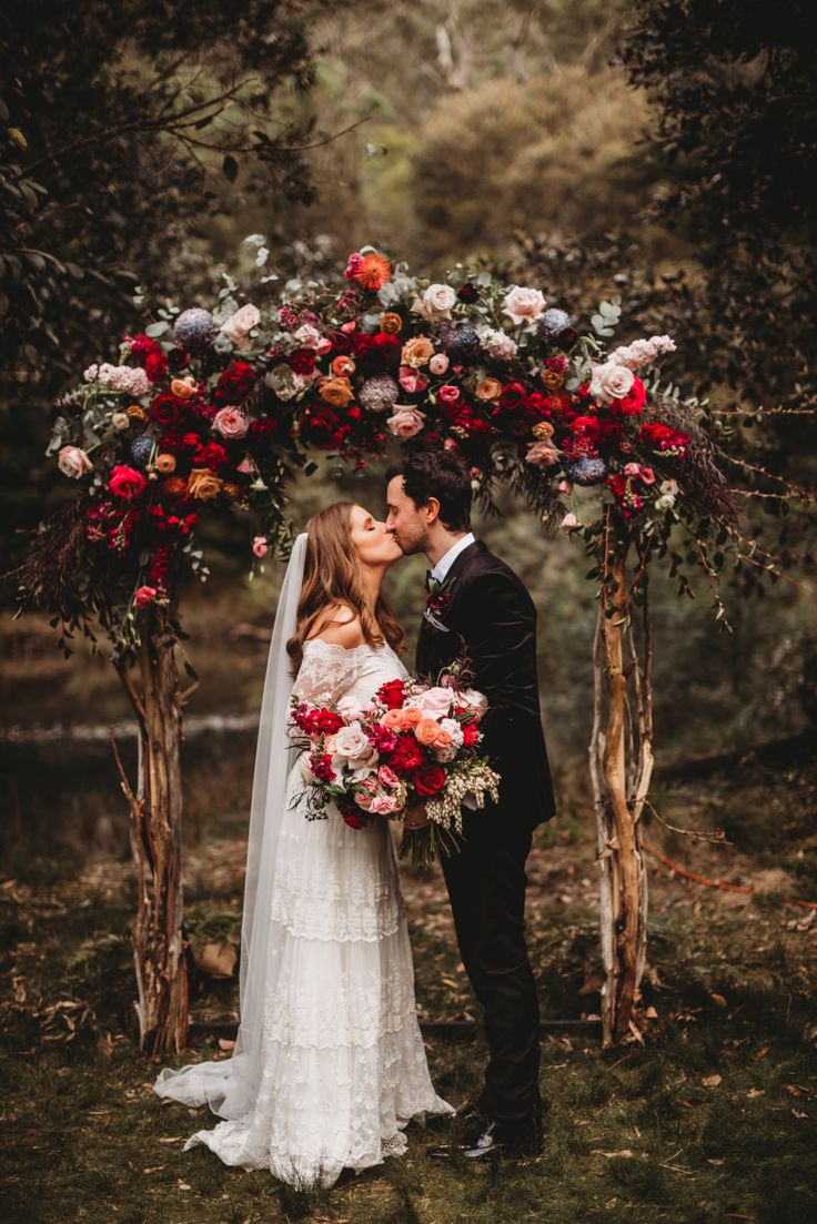 a bride and groom standing under an arch decorated with red, white and pink flowers