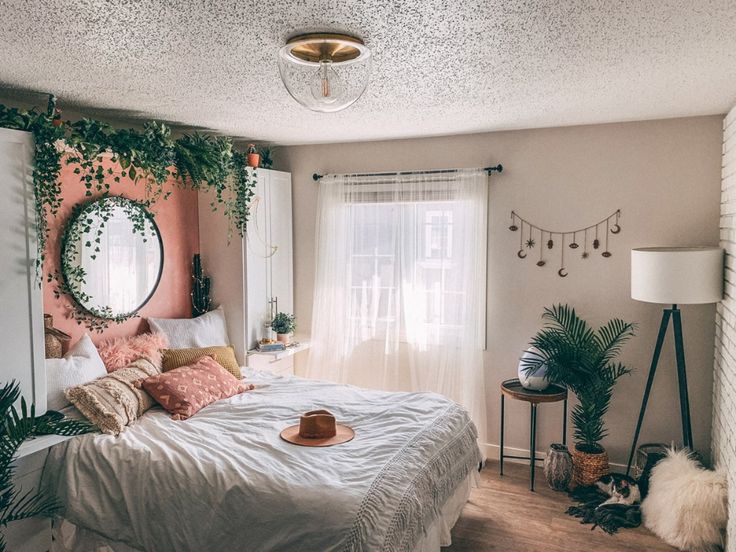 a bedroom decorated in pink and white with plants on the wall above the bed, along with a round mirror