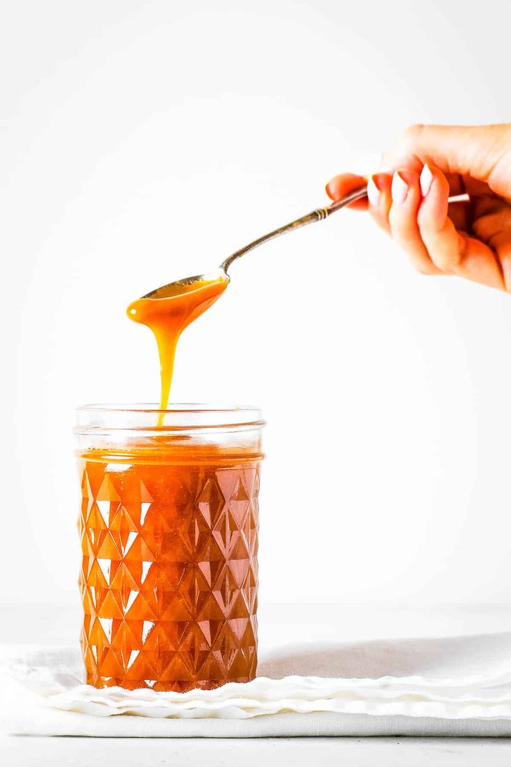 a person holding a spoon over a jar filled with orange liquid